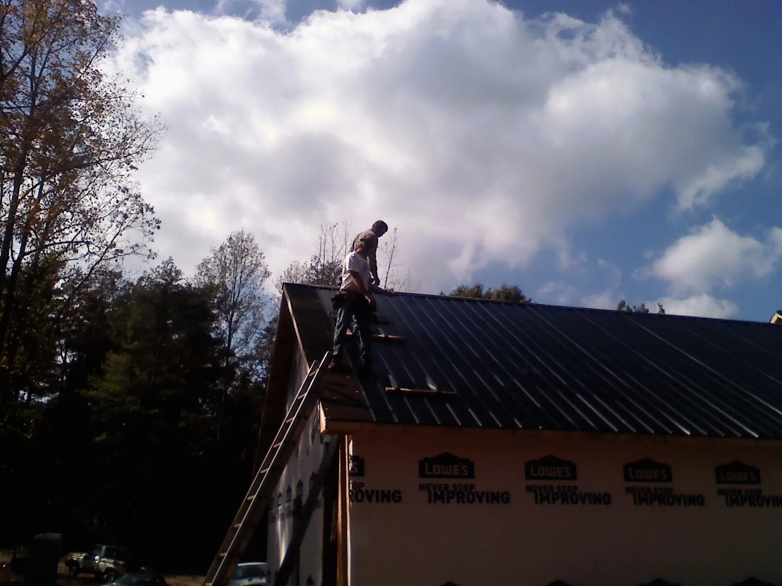 Roofer fastening dark metal panels high against a cloudy sky, from a Roof Inspection job in Colfax