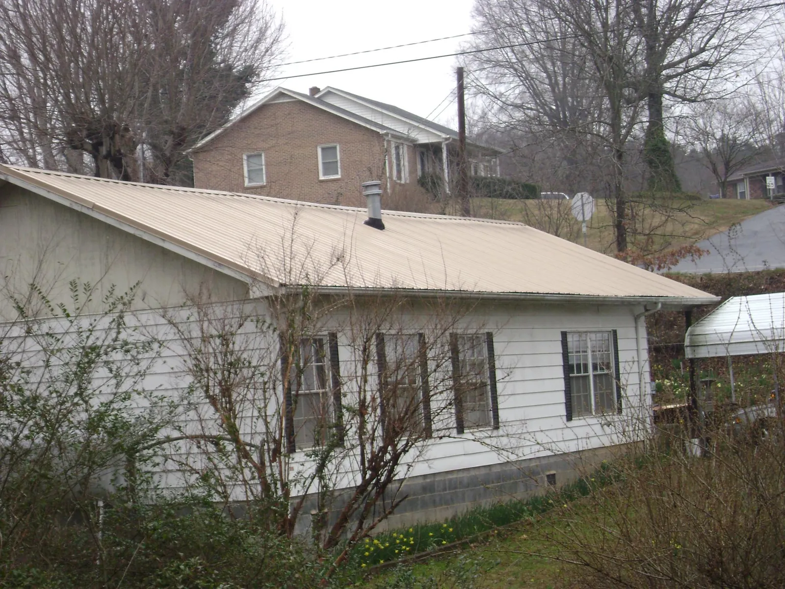 Tan metal roof on a white sided house set into a hillside — Commercial Roofing by Roofing Brothers in Colfax